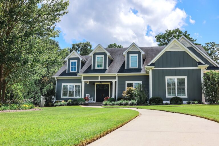 A low angle view of a large gray new construction house with a landscaped yard and leading pathway sidewalk.