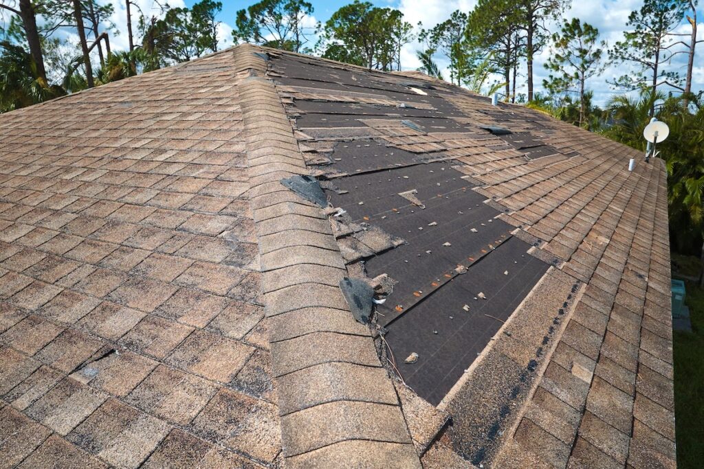 missing shingles Damaged house roof with missing shingles after hurricane Ian in Florida. Consequences of natural disaster.