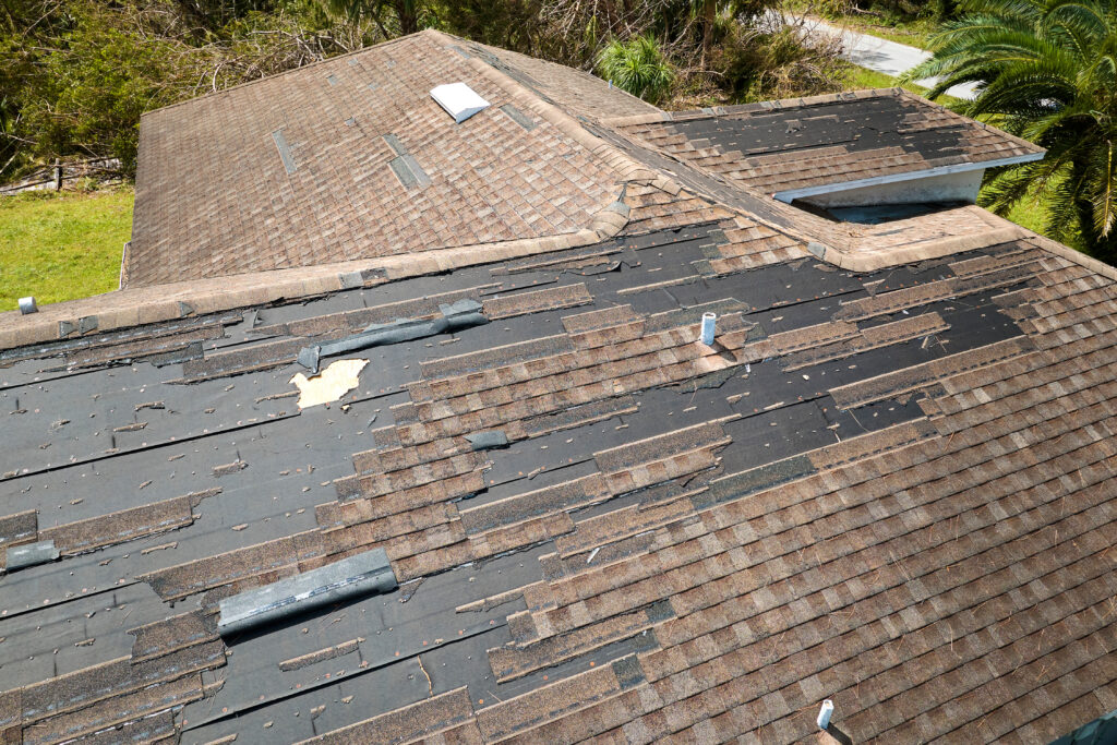 missing shingles Damaged house roof with missing shingles after hurricane Ian in Florida. Consequences of natural disaster.