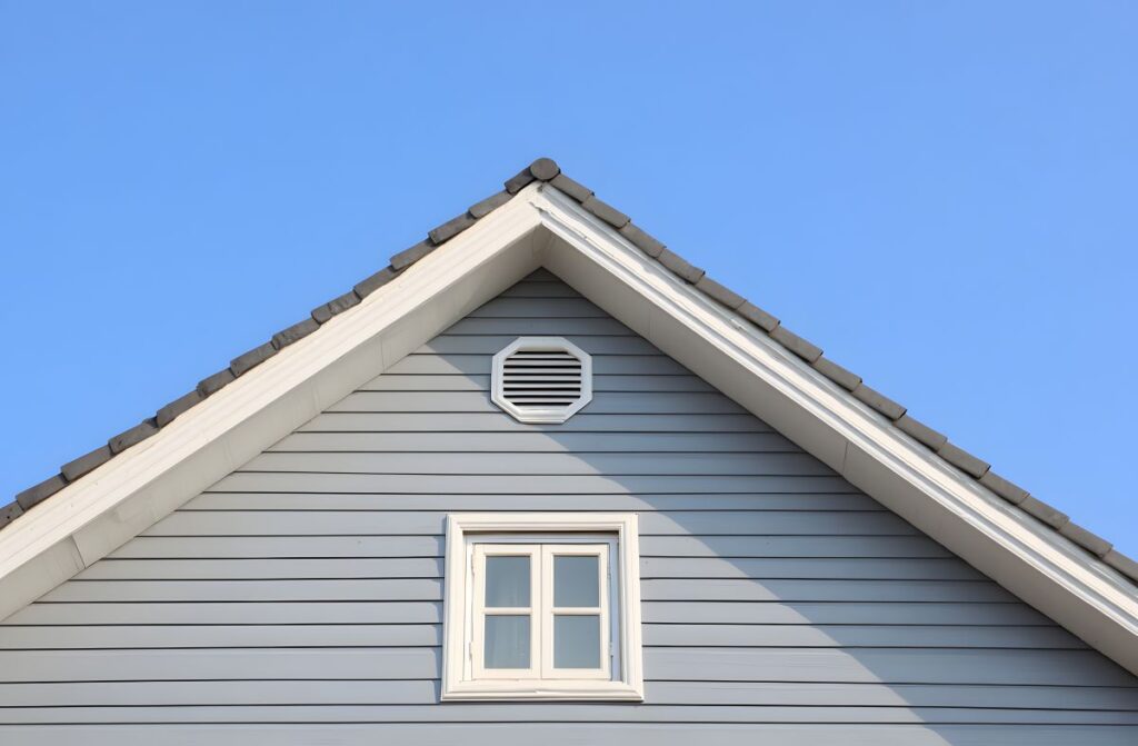 House exterior detail featuring peak of gable roof with gray vinyl siding white fascia