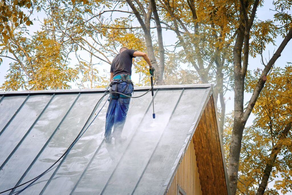 Man with pressure washer gun washing roof of private house